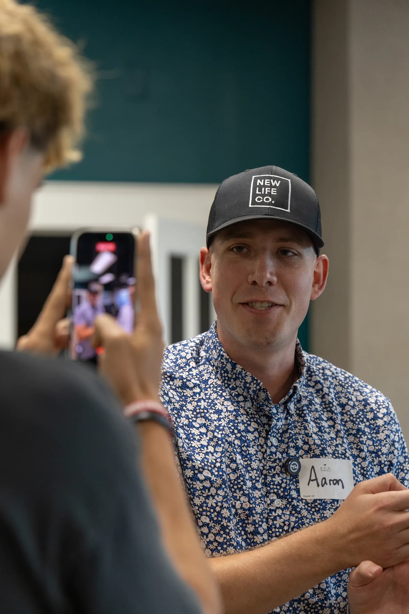 Aaron speaking while a person in the foreground records him on a phone